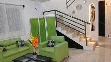 A modern living room with green sofas, a glass coffee table, and a staircase with a metal railing.