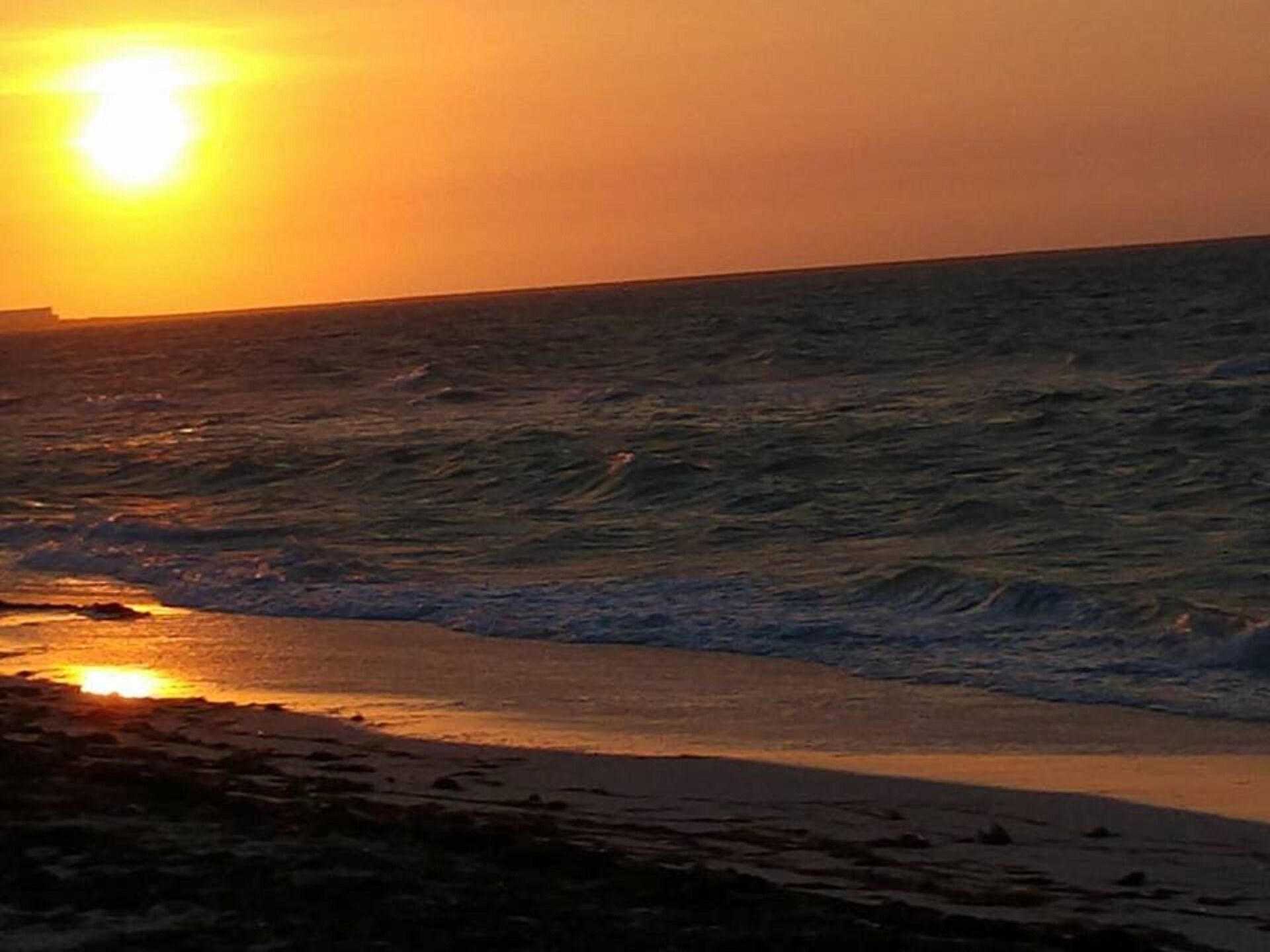 A beach with waves and a sunset.