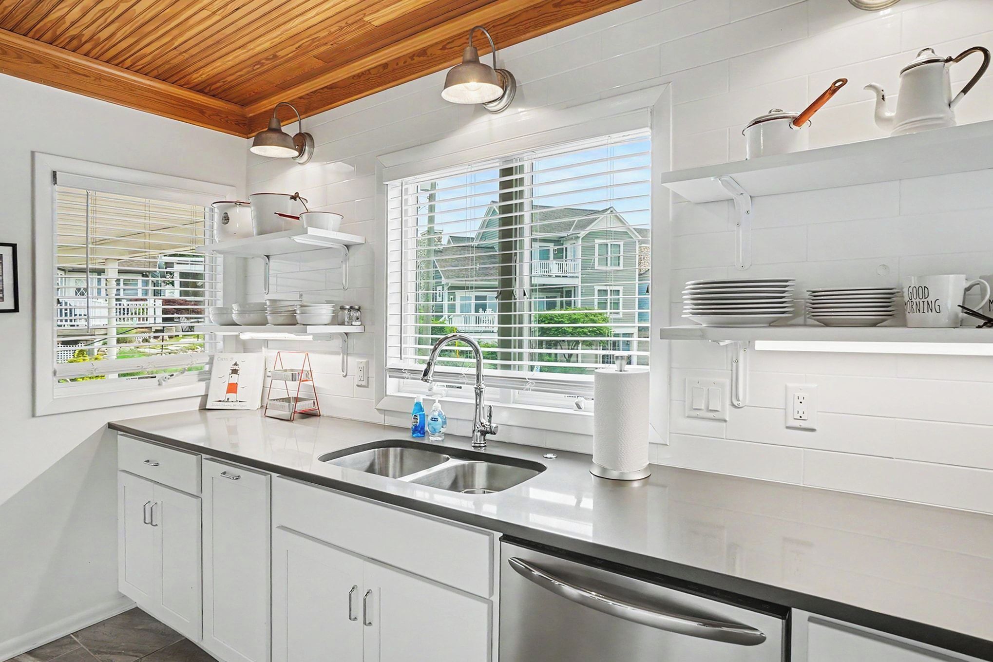 A modern kitchen with white cabinetry, stainless steel appliances, and a window with a view of houses.