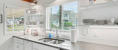 A modern kitchen with white cabinetry, stainless steel appliances, and a window with a view of houses.