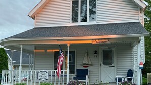 Een tweelaags huis met een veranda, een vlag en een bord waarop staat dat het te huur staat.