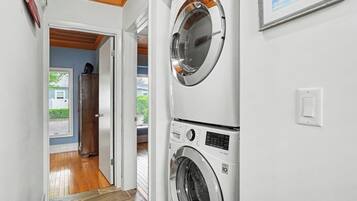 A laundry room with two stacked front-loading washing machines, a wooden door leading to a hallway, and a framed picture on the wall.