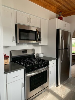 A modern kitchen with white cabinetry, a stainless steel microwave, a gas stove, and a refrigerator.