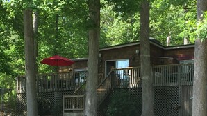 A wooden deck leading to a cabin with a red umbrella, surrounded by trees and a small stream. - Quiet cove, deep water, minutes to Clemson, pet friendly, easy path to the dock (Seneca)