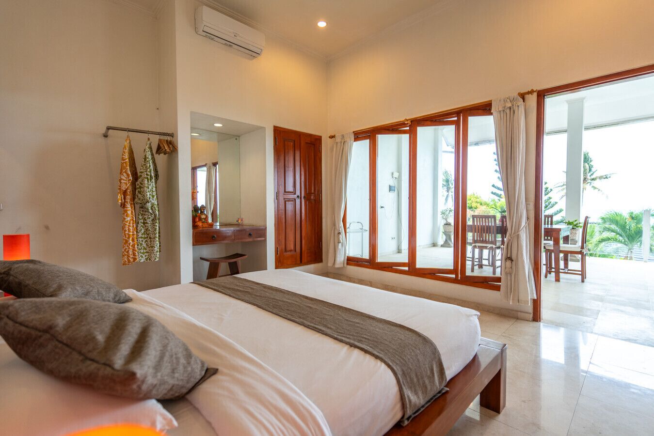 A bedroom with a large bed, a desk, and a view of the outdoor patio.