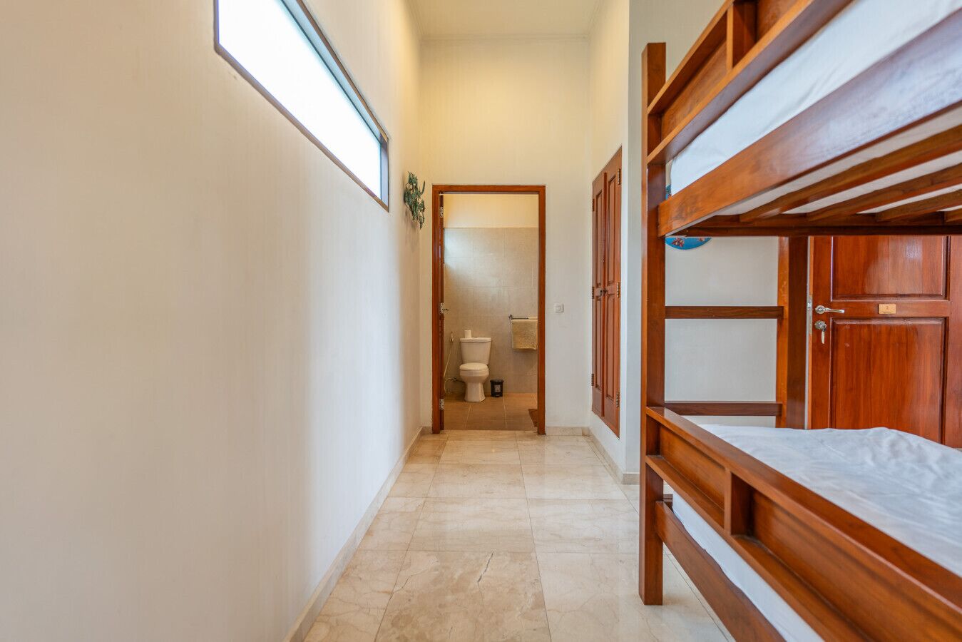 A narrow hallway with wooden bunk beds on one side and a door leading to a bathroom.