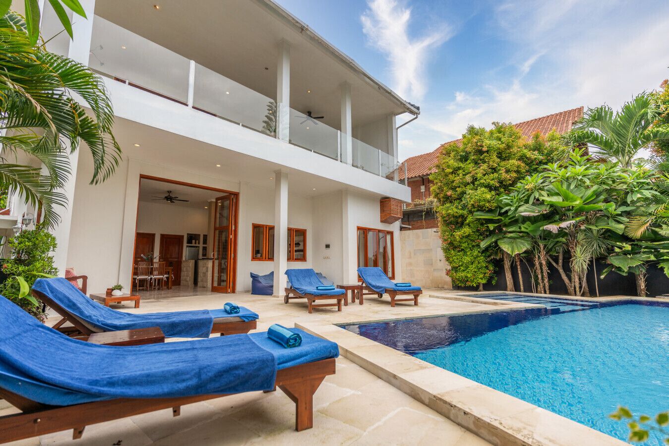 A modern villa with a swimming pool, sun loungers, and lush greenery.