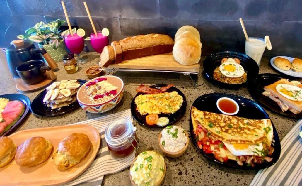 Una mesa de desayuno con diversos platos, entre ellos huevos, tostadas y pasteles.