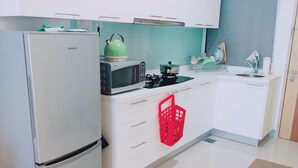 Cozinha compacta com geladeira, micro-ondas, chaleira e uma cesta vermelha.
