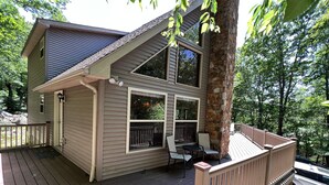 A two-story cabin with a deck, large windows, and a stone pillar. - Gorgeous Chalet in the Perfect Setting, Truly One of the Poconos Best (Lake Harmony)