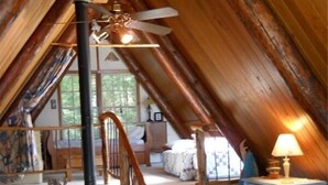Un dormitorio acogedor en el ático con una escalera de madera, una cama, un aparador y una lámpara.