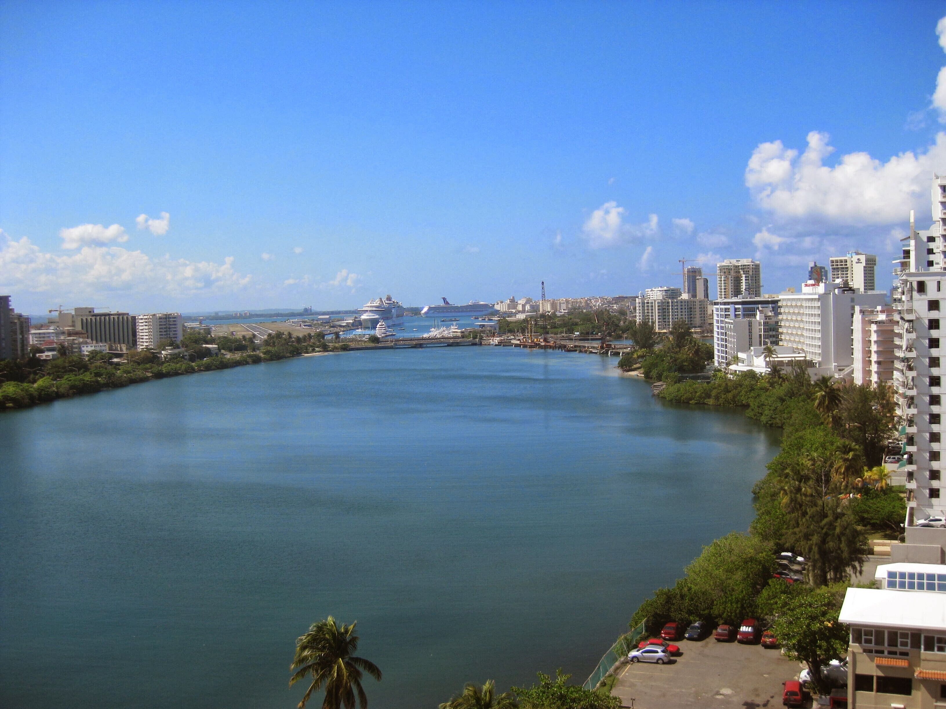 A river with buildings on both sides, a clear sky, and a distant cruise ship.