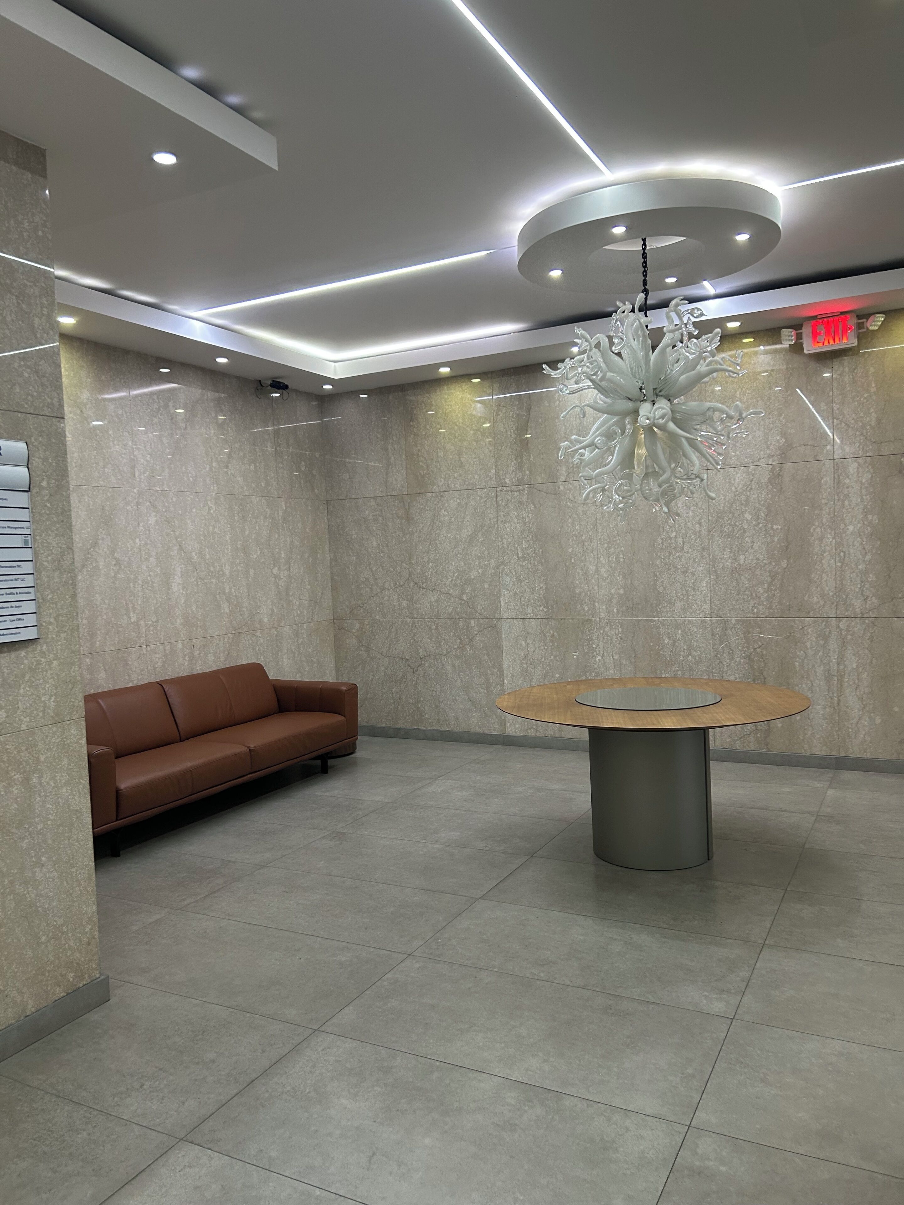 A lobby with a brown sofa, a round table, and a chandelier.