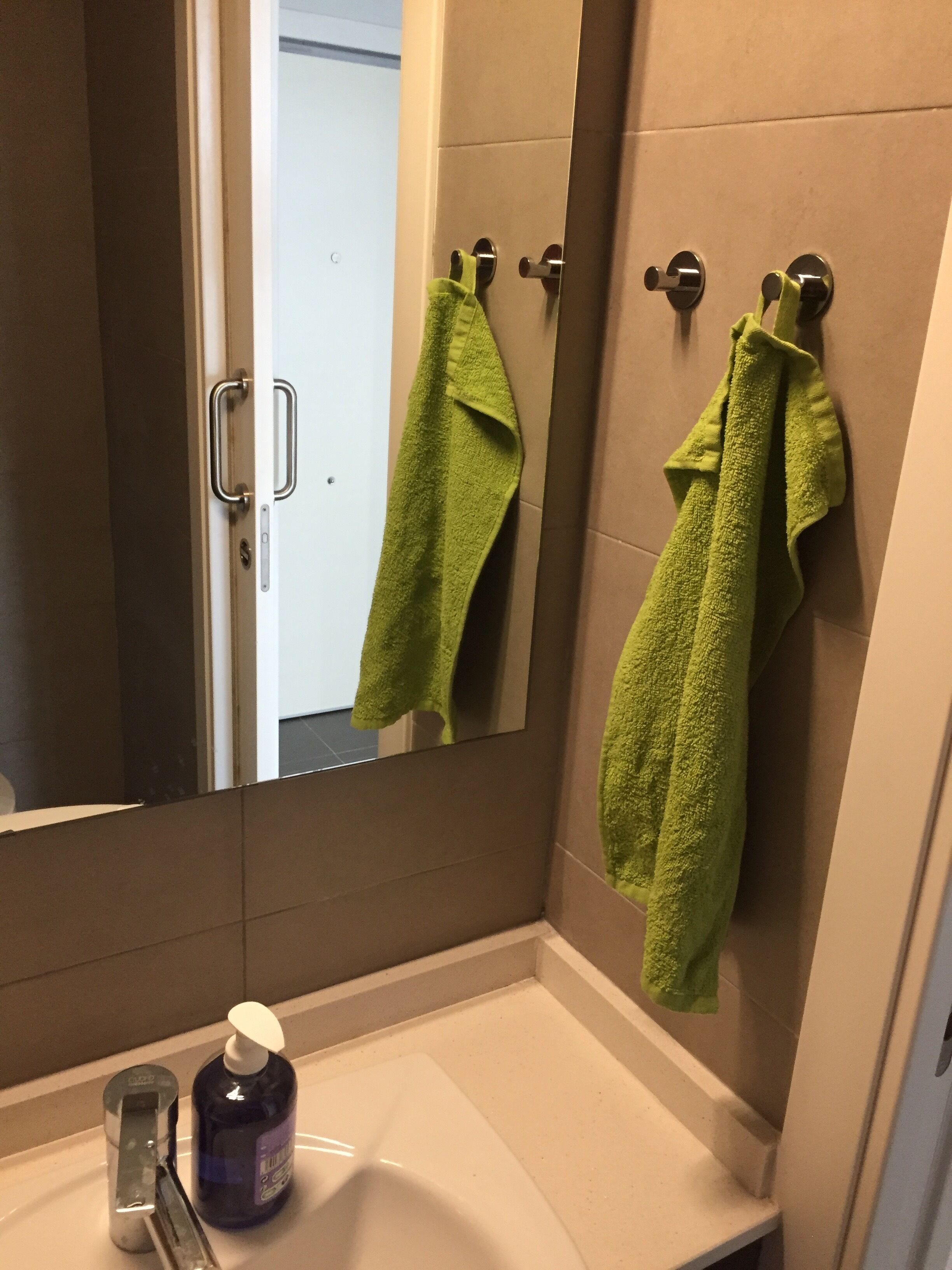 Un baño con un lavabo blanco, un espejo y dos toallas verdes colgadas en aros.