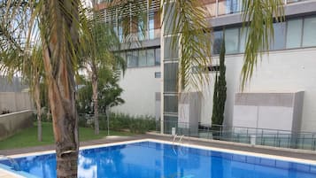 Una piscina rectangular con superficie de agua azul cristalina, rodeada por un deck de baldosas y un bajo borde de piedra.