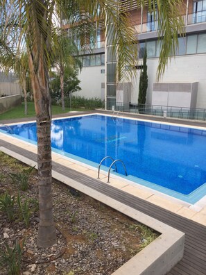 A rectangular swimming pool with a clear blue water surface, surrounded by a tiled deck and a low stone border. - Loft with terrace of 24m2, swimming pool, garden and garage. (València)