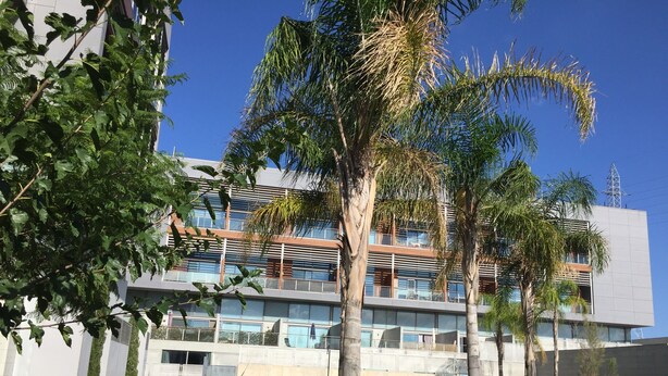 Um edifício moderno com vários andares, janelas amplas e área de piscina.
