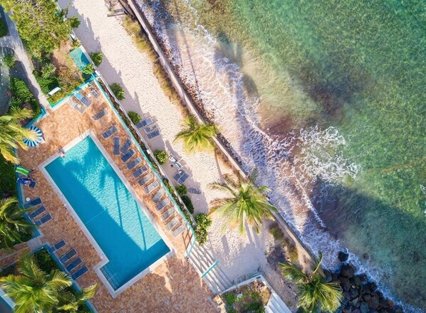 An aerial view of a resort with a swimming pool, beach, and palm trees.