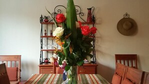 A dining table with a striped tablecloth, surrounded by wooden chairs. A vase with flowers is placed in the center.