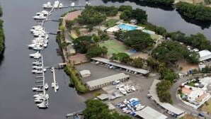 An aerial view of a marina with multiple boats docked, a swimming pool, and surrounding greenery.