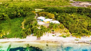 Une propriété située sur la côte, avec un bâtiment blanc, entourée d’une végétation luxuriante et donnant sur une plage.