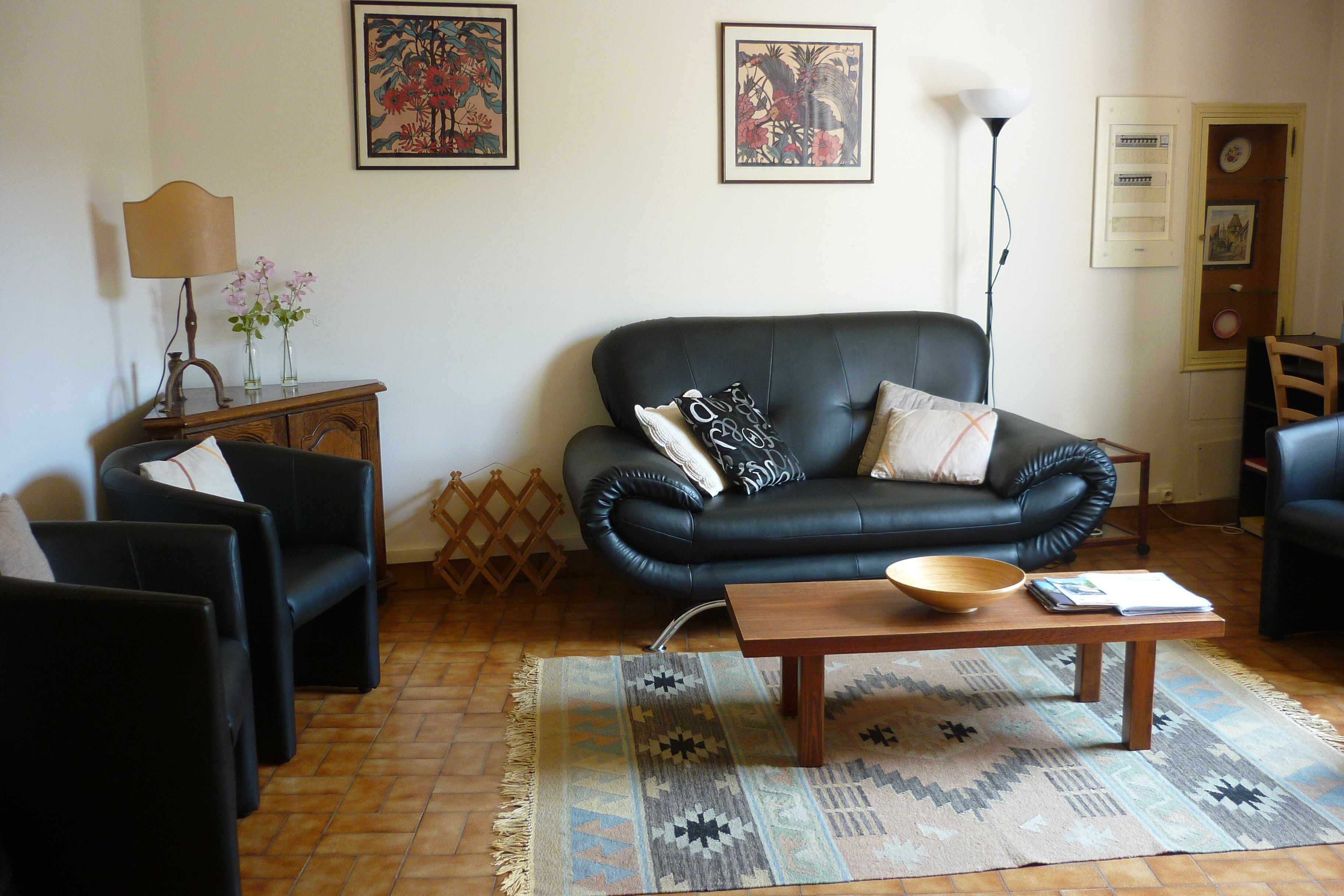 Una sala de estar con un sofá de cuero negro, dos sillones, una mesa de centro de madera y una alfombra estampada.