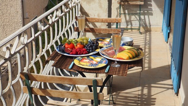 A balcony with a table set for a meal, including plates of fruit and a glass of wine. - Air-conditioned & heated cottage in picturesque Pernes-les-Fontaines (Pernes-les-Fontaines)