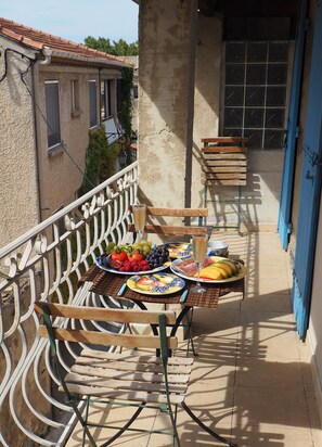 Un balcon avec une table dressée pour un repas, comprenant des assiettes de fruits et un verre de vin.