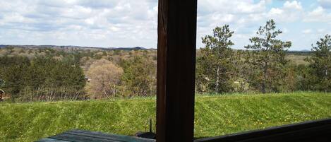 A view from a covered porch overlooking a grassy field with trees and distant hills.