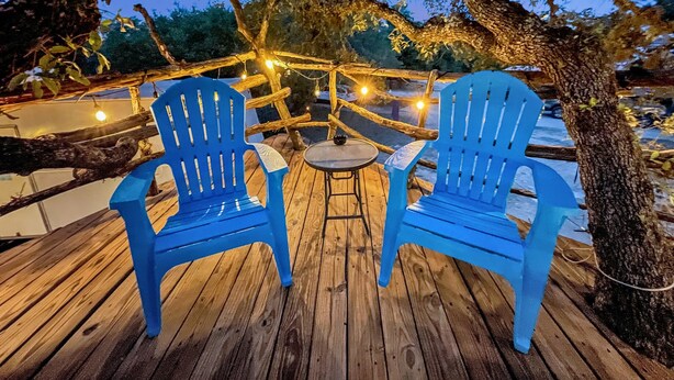 Une terrasse en bois avec deux chaises bleues et une petite table ronde, le tout illuminé par des guirlandes lumineuses.