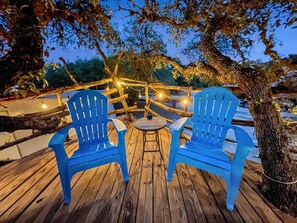 Une terrasse en bois avec deux chaises bleues et une petite table ronde, le tout illuminé par des guirlandes lumineuses.