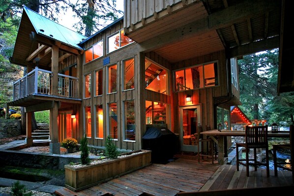 A multi-story wooden cabin with large windows, a deck, and a stone fireplace.