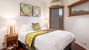 A neatly arranged hotel room with a bed, two bedside lamps, a nightstand, and a window with blinds. - Meko - Luxury Carlton House in Melbourne golden inner city (Carlton)
