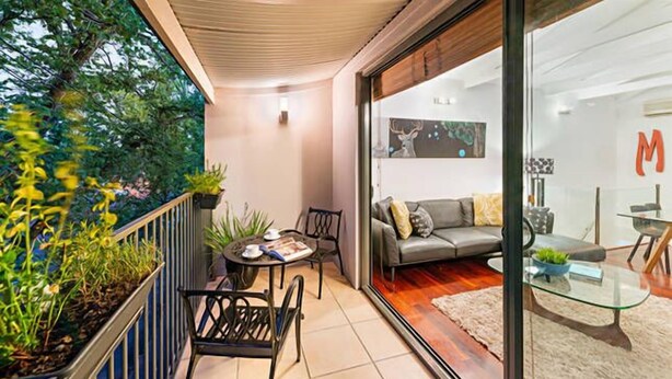 A modern living room with a grey sofa, a glass coffee table, and a dining area with a small table and chairs. - Meko - Luxury Carlton House in Melbourne golden inner city (Carlton)