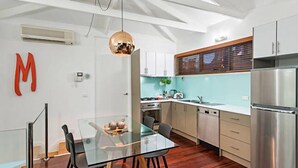 A modern kitchen with a glass dining table, stainless steel appliances, and a large 'M' on the wall. - Meko - Luxury Carlton House in Melbourne golden inner city (Carlton)