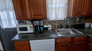 Una cocina compacta con armarios de madera, microondas, cafetera y lavabo.