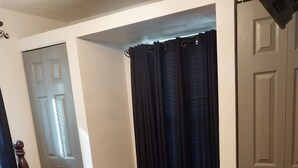Un dormitorio con cama, una silla, un ventanal con cortinas y una puerta.