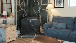 Un salon chaleureux avec une cheminée en pierre, un canapé bleu, une table basse en bois et une lampe.