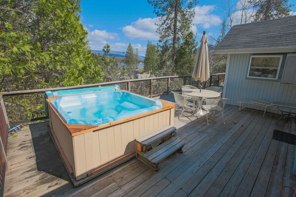 Une terrasse en bois avec un jacuzzi, du mobilier d’extérieur et une vue sur les arbres et les montagnes.