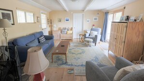 Un salon avec un canapé bleu, une table basse en bois et un fauteuil gris. On y trouve également un meuble en bois et une petite table avec une lampe.