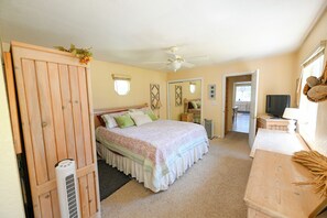 Une chambre à coucher comprenant un lit, un ventilateur de plafond, une commode et un téléviseur.