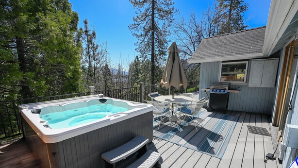 Un bain à remous sur une terrasse en bois, avec des meubles d’extérieur et un espace barbecue couvert.