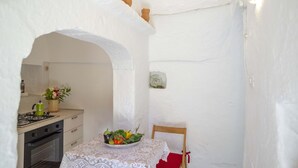 Eine Küche mit Herd, Backofen und Tisch, bedeckt mit einer Tischdecke aus Spitze, mit einer Obstschüssel darauf.