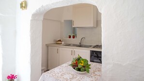 Eine Küche mit weißen Schränken, einer Spüle und einem Herd. Ein Tisch mit einer weißen Häkeldecke und eine Schüssel mit Obst.