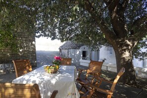An outdoor dining area with a table set for two, surrounded by wooden chairs, under a large tree. - Authentic And Lovely Trulli In Monopoli’s Countryside (Monopoli)