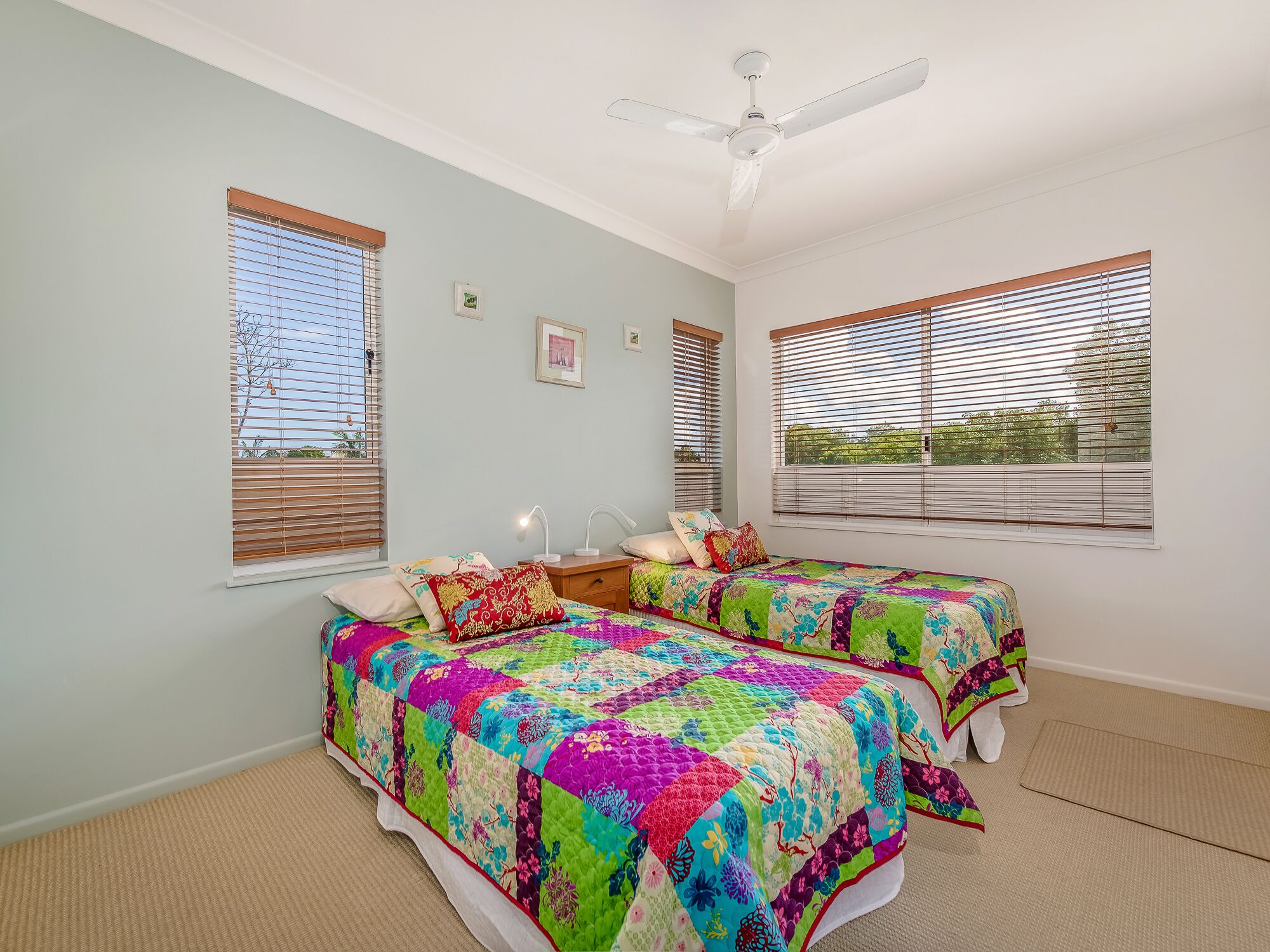 A bedroom with two beds, a ceiling fan, and large windows with blinds.