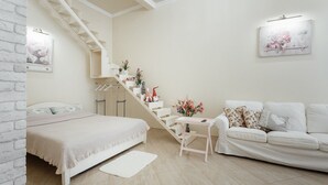Um quarto com cama, um sofá branco, uma mesinha, escada e prateleira com objetos decorativos.
