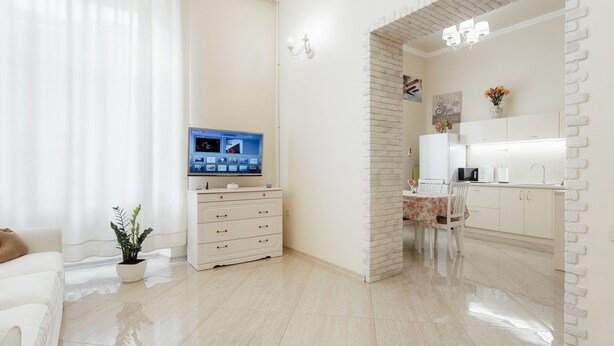 Uma sala de estar moderna com uma TV de tela plana, um sofá branco, uma mesa de centro e uma área de jantar com mesa e cadeiras.