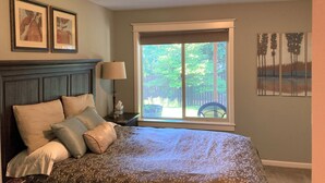A bedroom with a large bed, a nightstand, a lamp, and a window with a view of trees. - Spacious Single Party B&B – walking distance to downtown!  (Dundee)