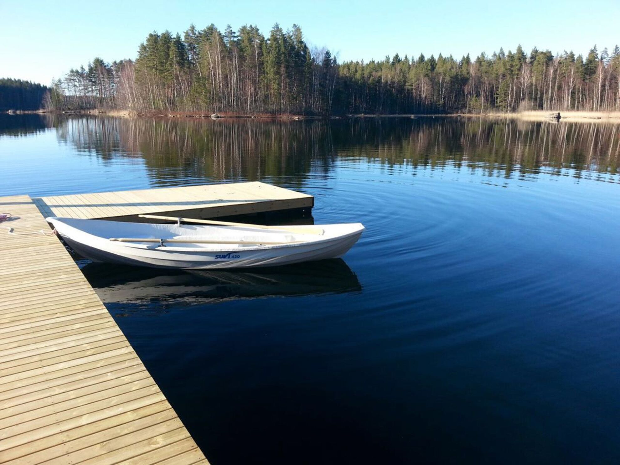 Un lac paisible, avec une jetée en bois et un petit bateau blanc amarré au quai.